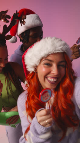 Vertical-Video-Studio-Shot-Of-Gen-Z-Friends-Dancing-And-Posing-For-Selfie-At-Christmas-Party-Wearing-Santa-Hat-And-Reindeer-Antlers-2